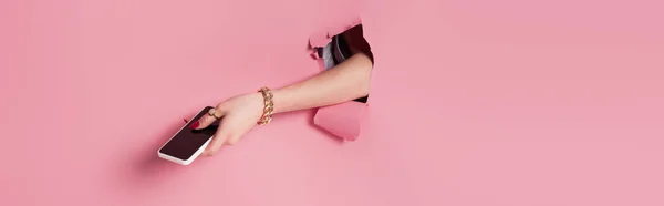 Vista ritagliata della donna che tiene lo smartphone nel foro di sfondo rosa, banner — Foto stock