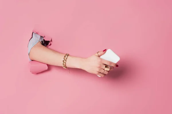 Cropped view of female hand with smartphone in hole in pink background — Stock Photo