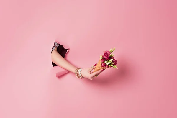 Ausgeschnittene Ansicht einer jungen Frau mit Rosen in Waffelkegel in der Nähe von rosa Hintergrund mit Loch — Stockfoto