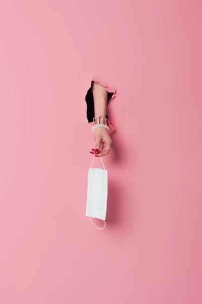 Vista ritagliata della donna che tiene la maschera medica nel foro di sfondo rosa — Foto stock