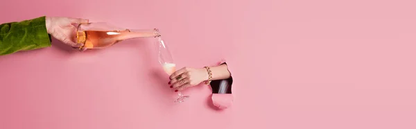 Vista recortada del hombre vertiendo champán cerca de la mujer con vidrio en el agujero de fondo rosa, pancarta - foto de stock