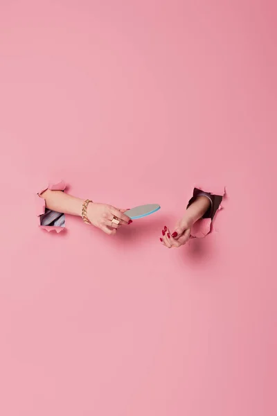 Cropped view of woman with red manicure holding nail file in holes of pink background — Stock Photo