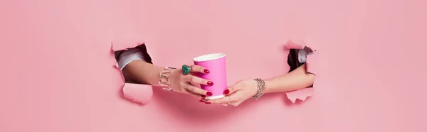 Cropped view of woman holding paper cup near pink background with holes, banner — Stock Photo