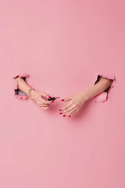 Vue recadrée de femme tenant applicateur avec vernis à ongles près de fond rose avec des trous — Photo de stock