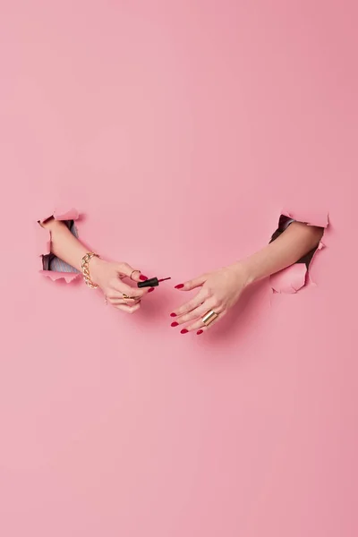 Cropped view of woman holding applicator with nail polish near pink background with holes — Stock Photo