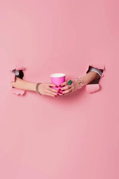 Cropped view of woman with accessories on hands holding takeaway drink near pink background with holes — Stock Photo