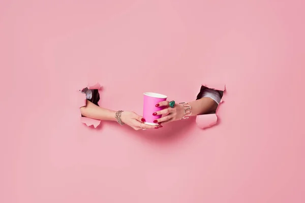 Cropped view of woman holding coffee to go in holes of pink background — Stock Photo