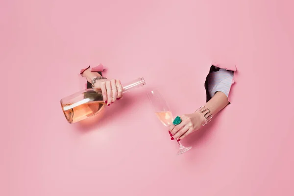 Vista cortada de mulher derramando champanhe em vidro em buracos de fundo rosa — Fotografia de Stock