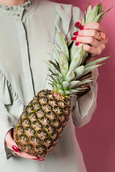 Cropped view of young woman holding exotic pineapple on pink background — Stock Photo