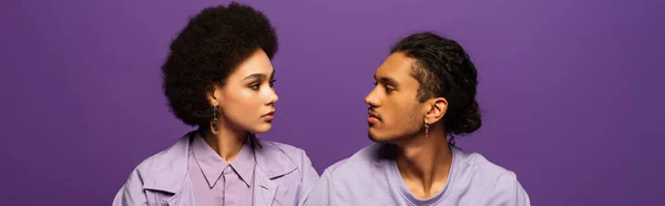 African american man and curly young woman looking at each other isolated on purple, banner — Stock Photo