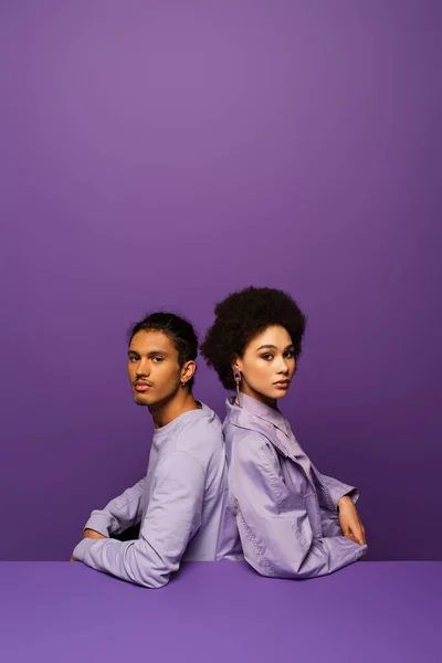 Couple afro-américain à la mode assis dos à dos isolé sur violet — Photo de stock