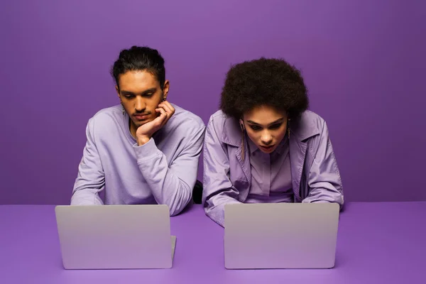Joven afroamericano hombre y mujer usando ordenadores portátiles aislados en púrpura - foto de stock