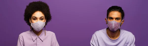 Young african american man and woman in protective masks isolated on purple, banner — Stock Photo