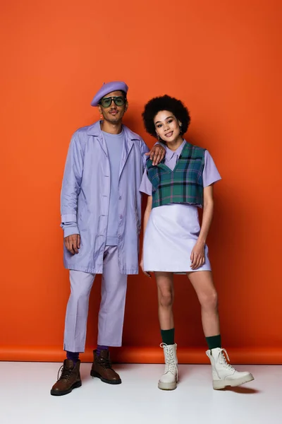 Longitud completa de hombre y mujer afroamericanos de moda sonriendo mientras posan en naranja - foto de stock