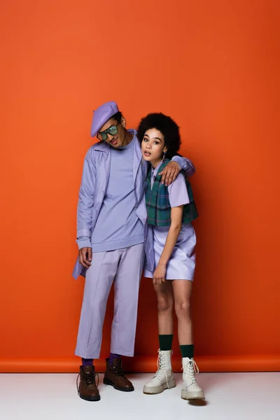 Comprimento total de homem americano africano na moda sorrindo enquanto posando com mulher encaracolada em laranja — Fotografia de Stock