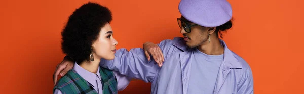 Homme afro-américain à la mode en béret et femme se regardant sur orange, bannière — Photo de stock