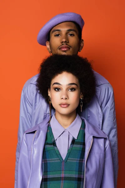 Curly woman in purple jacket near stylish man in beret isolated on orange — Stock Photo