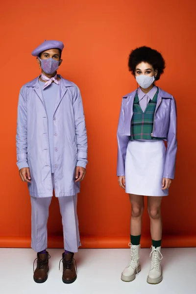 Piena lunghezza di trendy coppia afroamericana in maschere protettive su arancione — Foto stock