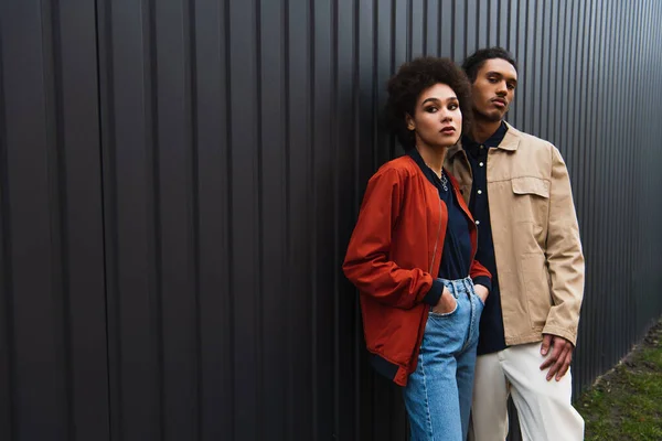 African american man looking at camera while posing with curly woman in jeans outside — Stock Photo