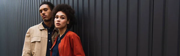 African american man looking at camera while posing with curly woman in orange jacket, banner — Stock Photo