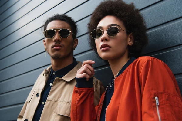 Jeune homme afro-américain posant avec une femme bouclée dans des lunettes de soleil à l'extérieur — Photo de stock