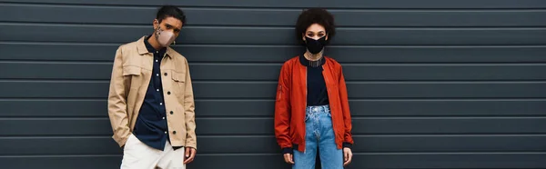 Jovem mulher americana africana e homem elegante em máscaras protetoras posando fora, bandeira — Fotografia de Stock