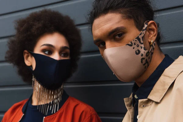 Donna afroamericana offuscata e l'uomo alla moda in maschere protettive posa al di fuori — Foto stock