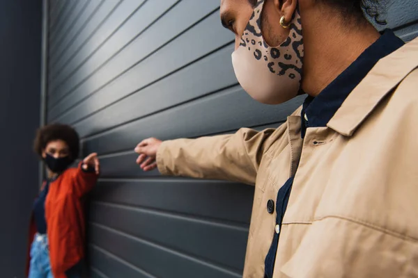 Молодой африканский американец и размытая женщина в стильных защитных масках с протянутыми руками — стоковое фото