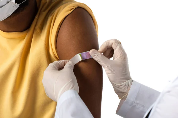 Vista recortada del médico que aplica yeso adhesivo en el brazo del paciente afroamericano aislado en blanco - foto de stock