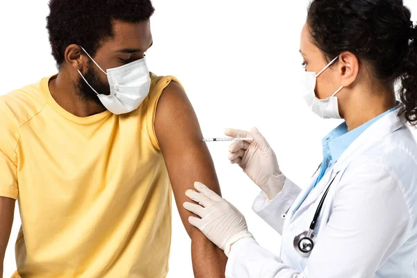 Medico afroamericano in maschera protettiva e guanti di lattice che fa la vaccinazione di paziente isolato su bianco — Foto stock