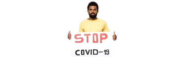 Hombre afroamericano sosteniendo pancarta con letras stop covid-2019 aisladas en blanco, pancarta - foto de stock