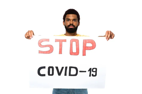 Африканский американец с надписью Stop covid-2019 на плакате смотрит на камеру, изолированную на белом — стоковое фото