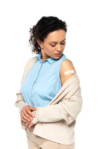 Mujer afroamericana mirando yeso adhesivo en el brazo aislado en blanco - foto de stock