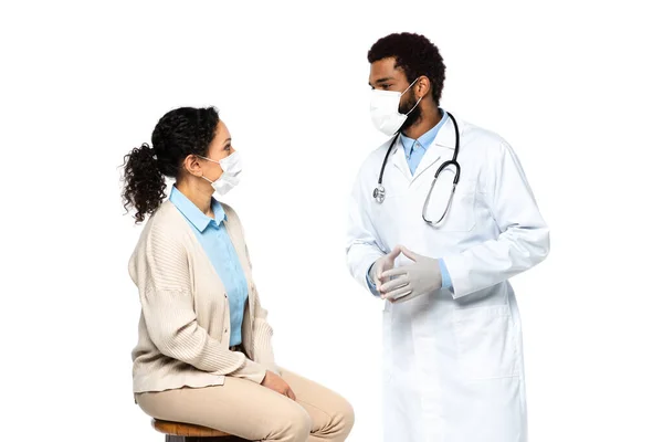 Médico afroamericano en máscara médica hablando con paciente aislado en blanco - foto de stock