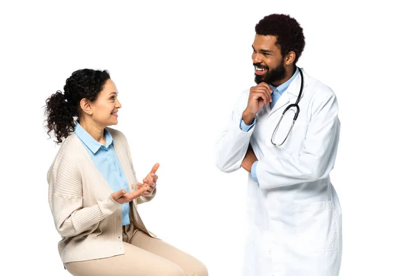 Paciente afro-americano sorridente conversando com médico de avental branco isolado em branco — Fotografia de Stock