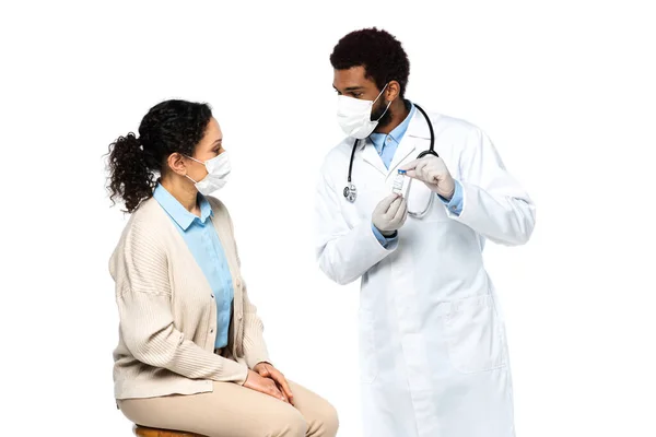 Médecin afro-américain dans des gants en latex tenant le pot avec le vaccin près du patient isolé sur blanc — Photo de stock