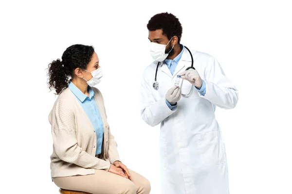 Médico afro-americano em luvas de látex segurando frasco com vacina perto do paciente isolado em branco — Fotografia de Stock