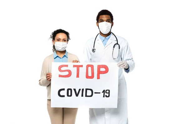 Médico afroamericano y paciente sosteniendo pancarta con letras stop covid-2019 aisladas en blanco - foto de stock