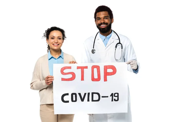 Cartel de paciente afroamericano sonriente y médico con cartelera de stop covid-2019 aislado en blanco - foto de stock