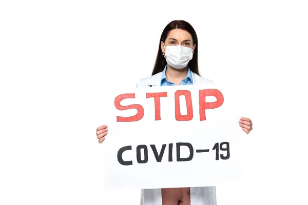 Doctor en bata blanca y máscara protectora sosteniendo pancarta con letras stop covid-2019 aisladas en blanco - foto de stock