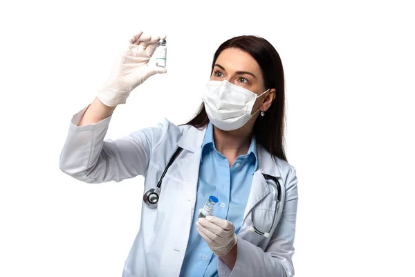 Médico morena em máscara médica olhando para a vacina isolada em branco — Fotografia de Stock
