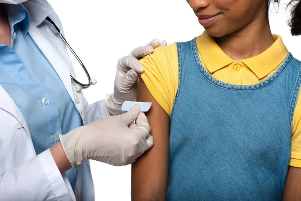Vista ritagliata del medico che applica intonaco adesivo sul braccio del bambino afroamericano isolato su bianco — Foto stock