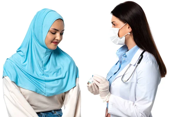 Врач в медицинской маске держит вакцину рядом с арабским пациентом изолированы на белом — стоковое фото