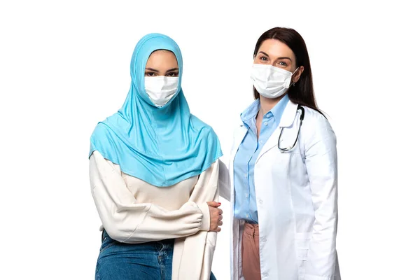Мусульманский пациент и врач в медицинских масках, смотрящий на камеру, изолированную на белом — стоковое фото