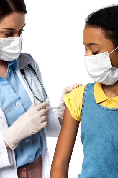 Doctor doing injection with vaccine to african american kid in medical mask isolated on white — Stock Photo