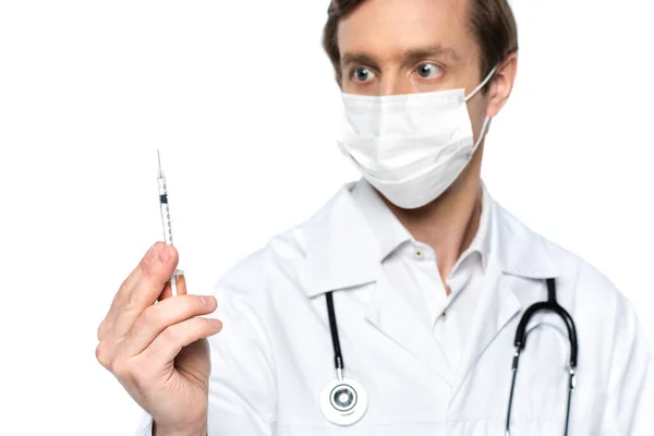 Шприц с вакциной в руке врача в медицинской маске на размытом фоне изолирован на белом — стоковое фото
