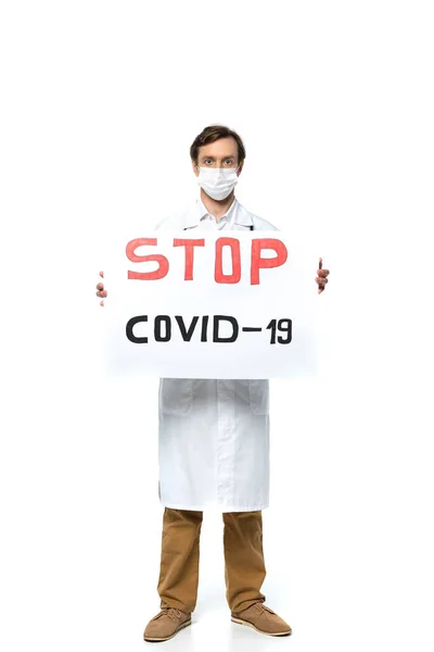 Doctor en bata blanca y máscara protectora sosteniendo pancarta con letras stop covid-2019 sobre fondo blanco - foto de stock