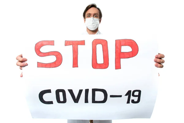 Placard con letras stop covid-2019 en manos de médico borroso en máscara médica aislado en blanco - foto de stock