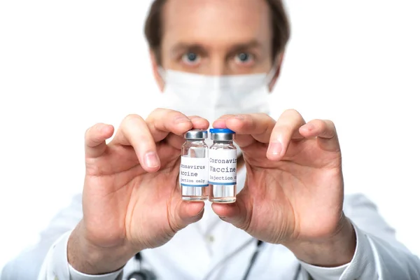 Jars with coronavirus lettering on vaccine in hands of blurred doctor isolated on white — Stock Photo