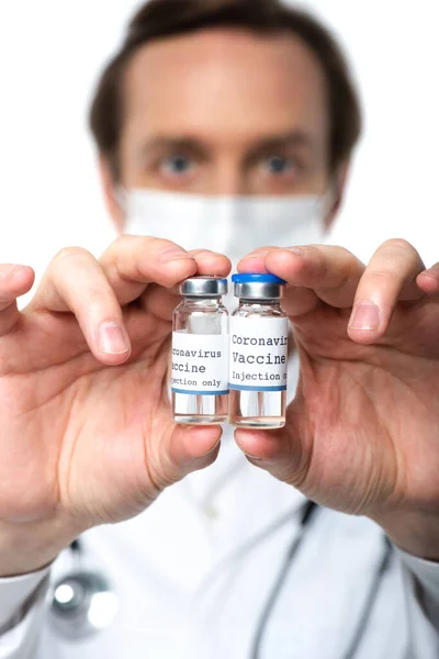 Letras de la vacuna contra el Coronavirus en frascos en manos del médico en máscara médica sobre fondo borroso aislado en blanco — Stock Photo